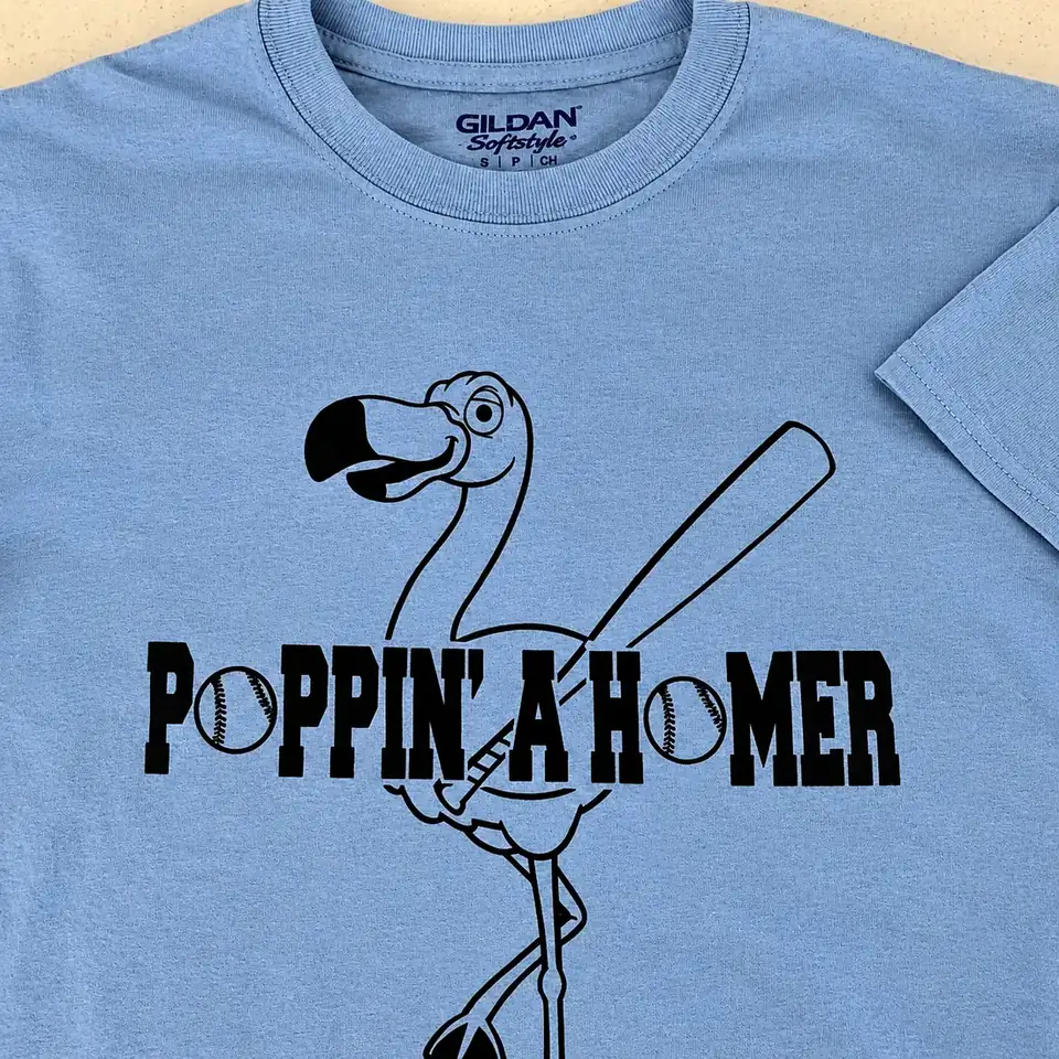 Light blue T-shirt printed with a baseball-playing flamingo and the words Poppin' a Homer